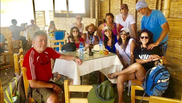 A group of people seated at a table under a bamboo roofed area with chairs and tables arranged for dining.
