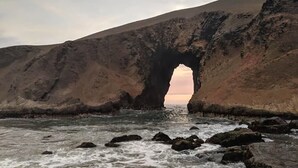A natural rock formation with a cave-like opening at the water's edge.