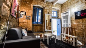 A rustic room with stone walls, a black leather sofa, a small table, and a blue door. - Historic Townhouse in Birgu Center (Il-Birgu)