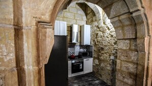A narrow stone-walled kitchen with a modern stove, white cabinets, and a tiled backsplash. - Historic Townhouse in Birgu Center (Il-Birgu)
