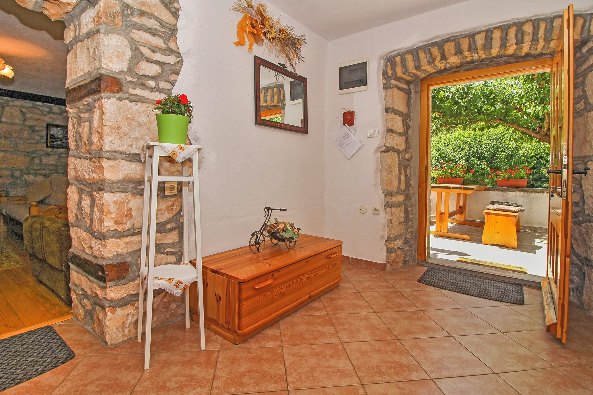 Una entrada de paredes de piedra con un banco de madera, una mesita con una planta en maceta y un espejo en la pared.