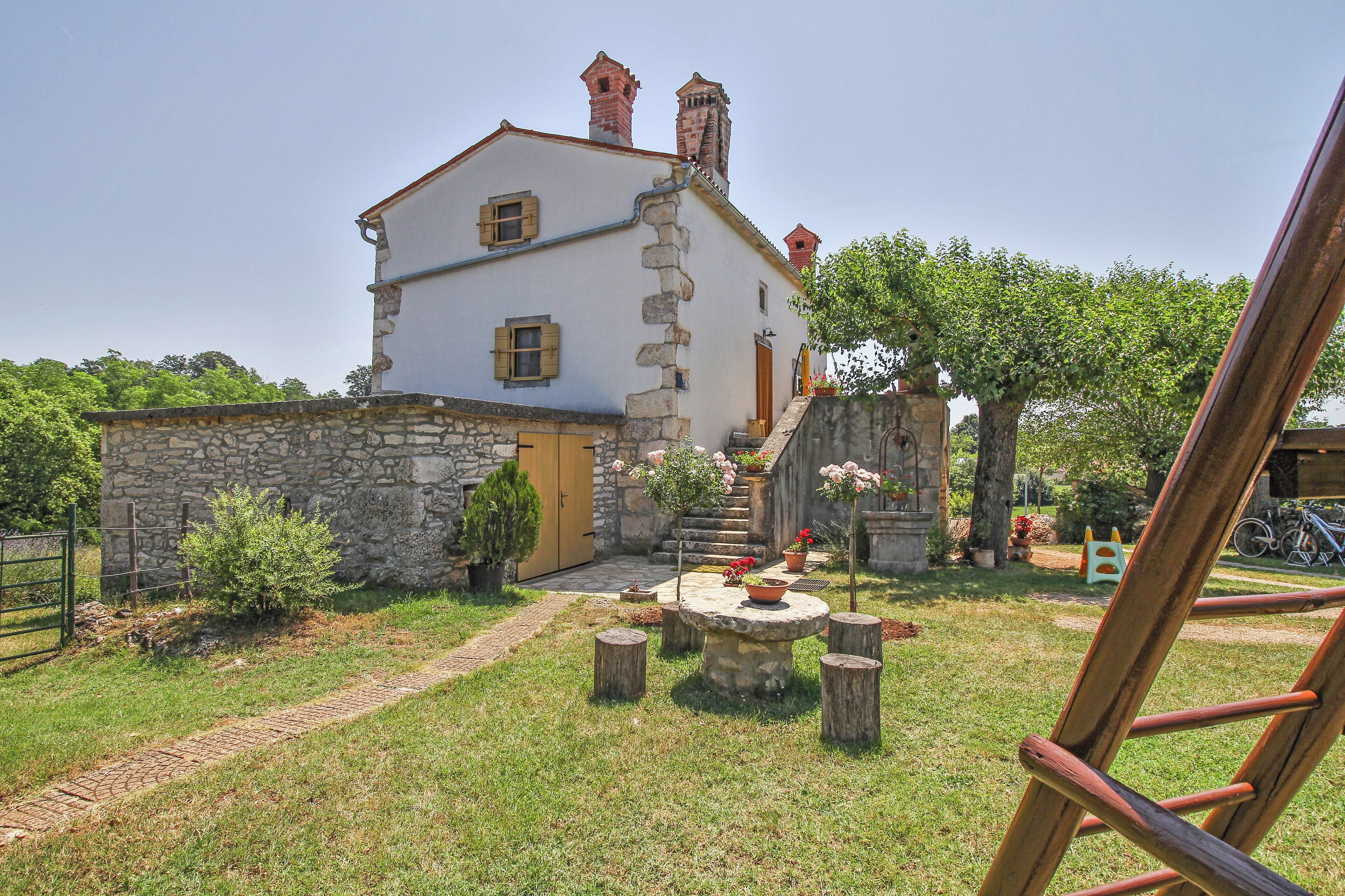 Un bâtiment en pierre avec une façade blanche, une porte en bois et un petit jardin agrémenté d’une table et de chaises.