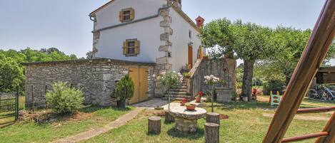 Un bâtiment en pierre avec une façade blanche, une porte en bois et un petit jardin agrémenté d’une table et de chaises.