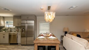 A modern kitchen with stainless steel appliances, a wooden dining table set for two, and a cozy living area with a sofa and lamp. - Updated East Boca House (Boca Raton)