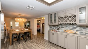 A modern kitchen with a wooden dining table, bar stools, and a Ti Punch Bar sign. - Updated East Boca House (Boca Raton)