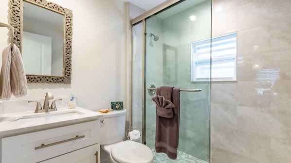 Un bany modern amb plat de dutxa de vidre, un lavabo blanc i un gran mirall amb una estructura decorativa.