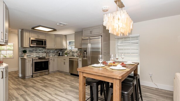 A modern kitchen with stainless steel appliances, a wooden dining table set for four, and a chandelier. - Updated East Boca House (Boca Raton)
