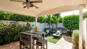 A covered patio with a table and chairs, surrounded by lush greenery and a white fence. - Updated East Boca House (Boca Raton)