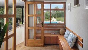 Ein Zimmer mit einer Holzbank, einer gepolsterten Bank, einer Holztür und Blick auf einen Swimmingpool.