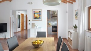 Ein geräumiger Wohnbereich mit Esstisch, Stühlen, einem Fernseher und einer Küche im Hintergrund.
