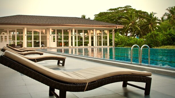 Un espace aménagé au bord de la piscine, avec des chaises longues, et un bâtiment doté de grandes fenêtres.
