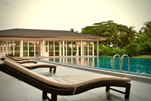 A poolside area with lounge chairs and a building with large windows. - Grandiose Fairway Galle (Galle)