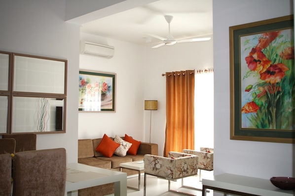 A living room with a sofa, armchairs, a coffee table, a floor lamp, and a painting on the wall.