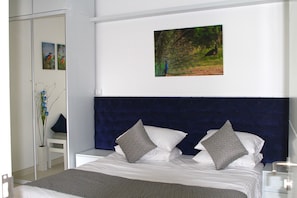 A neatly arranged bedroom with a large bed, two pillows, a dark headboard, and a framed picture on the wall.