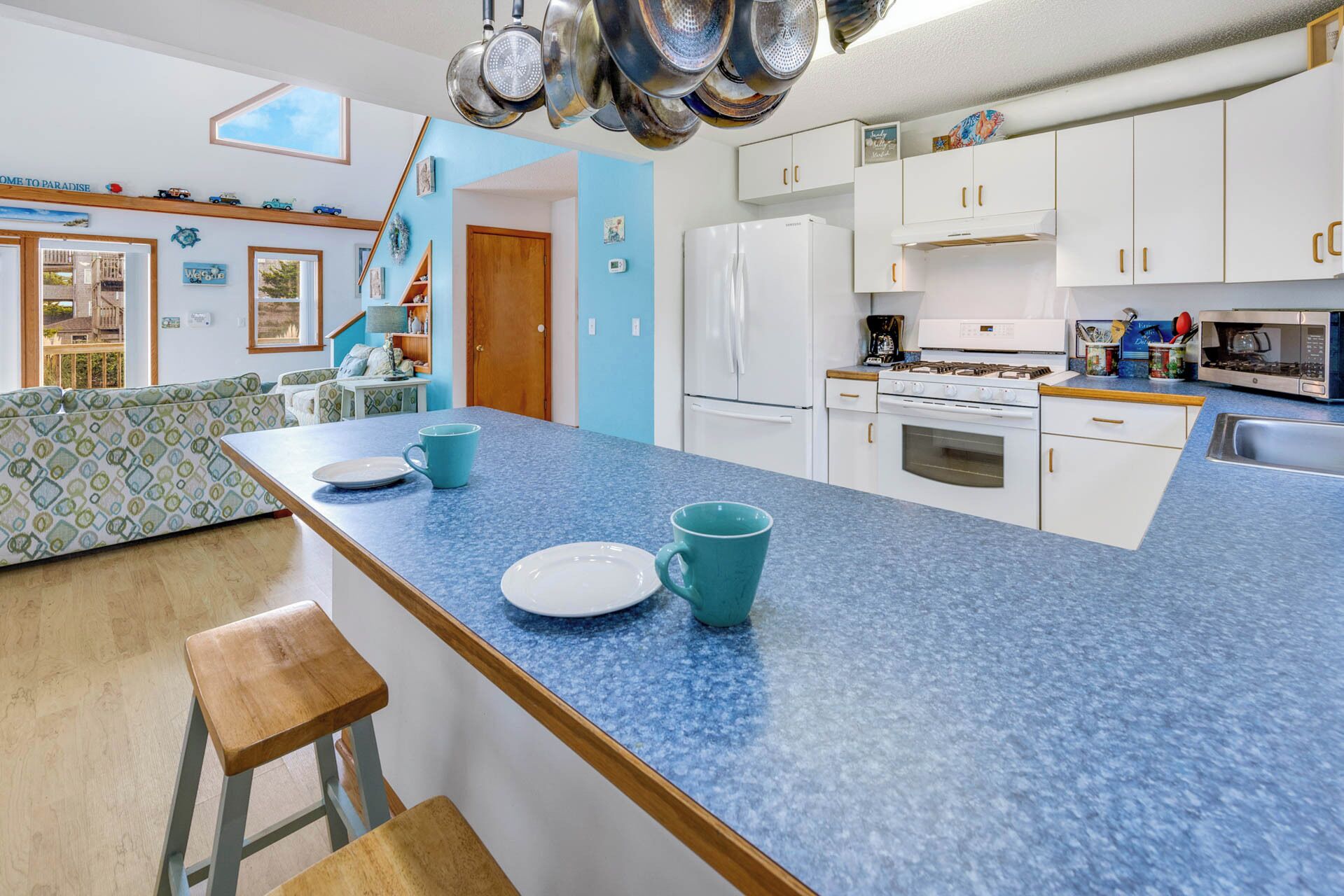 Eine moderne Küche mit blauer Arbeitsplatte, weißen Schränken und einem Gasherd. Es gibt einen Essbereich mit einem blauen Sofa und einem Holzhocker.