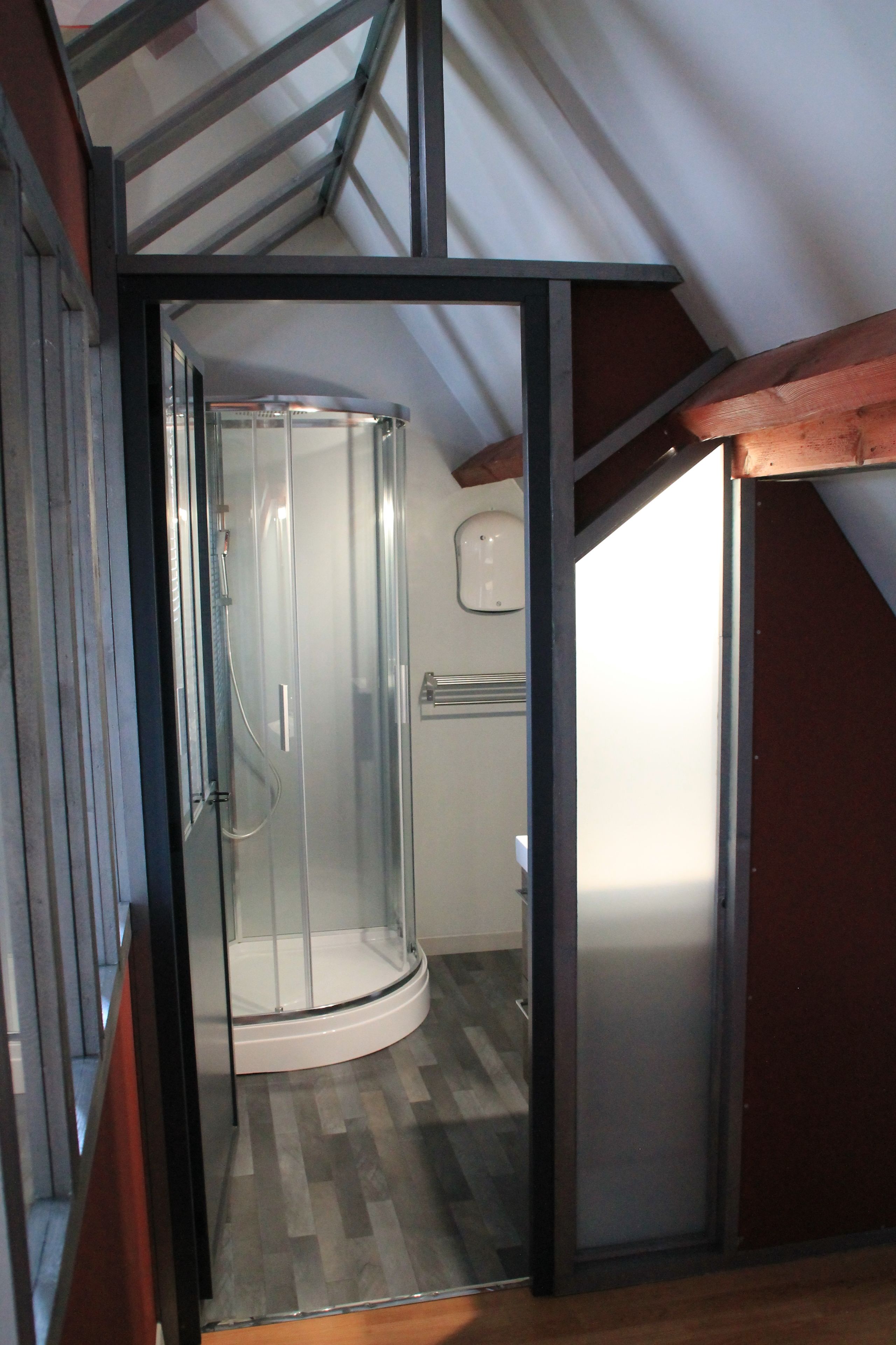 A glass-enclosed shower area with a curved design, a wooden floor, and a metal frame structure.