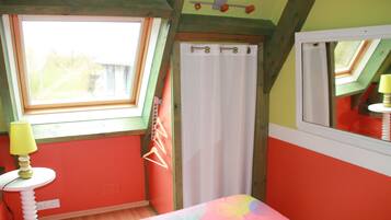 A bedroom with a skylight, a bed with a colorful bedspread, a bedside table with a lamp, and a window with a curtain.