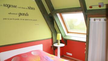 A room with a sloped ceiling, a bed with a colorful bedspread, a small table with a lamp, and a window with a curtain.