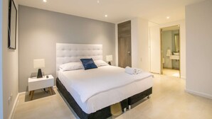 A modern bedroom with a large bed, bedside tables, and a bathroom visible through an open door. - 1 BR Beautiful New Apartment in Bocagrande (Cartagena)