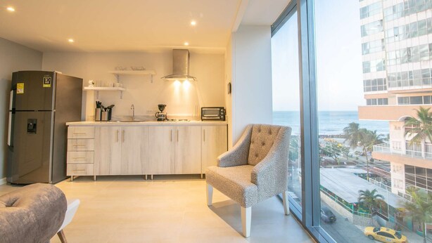 A modern kitchen with a built-in oven, microwave, and coffee maker. There is a large window offering a view of the city and the ocean. - 1 BR Beautiful New Apartment in Bocagrande (Cartagena)