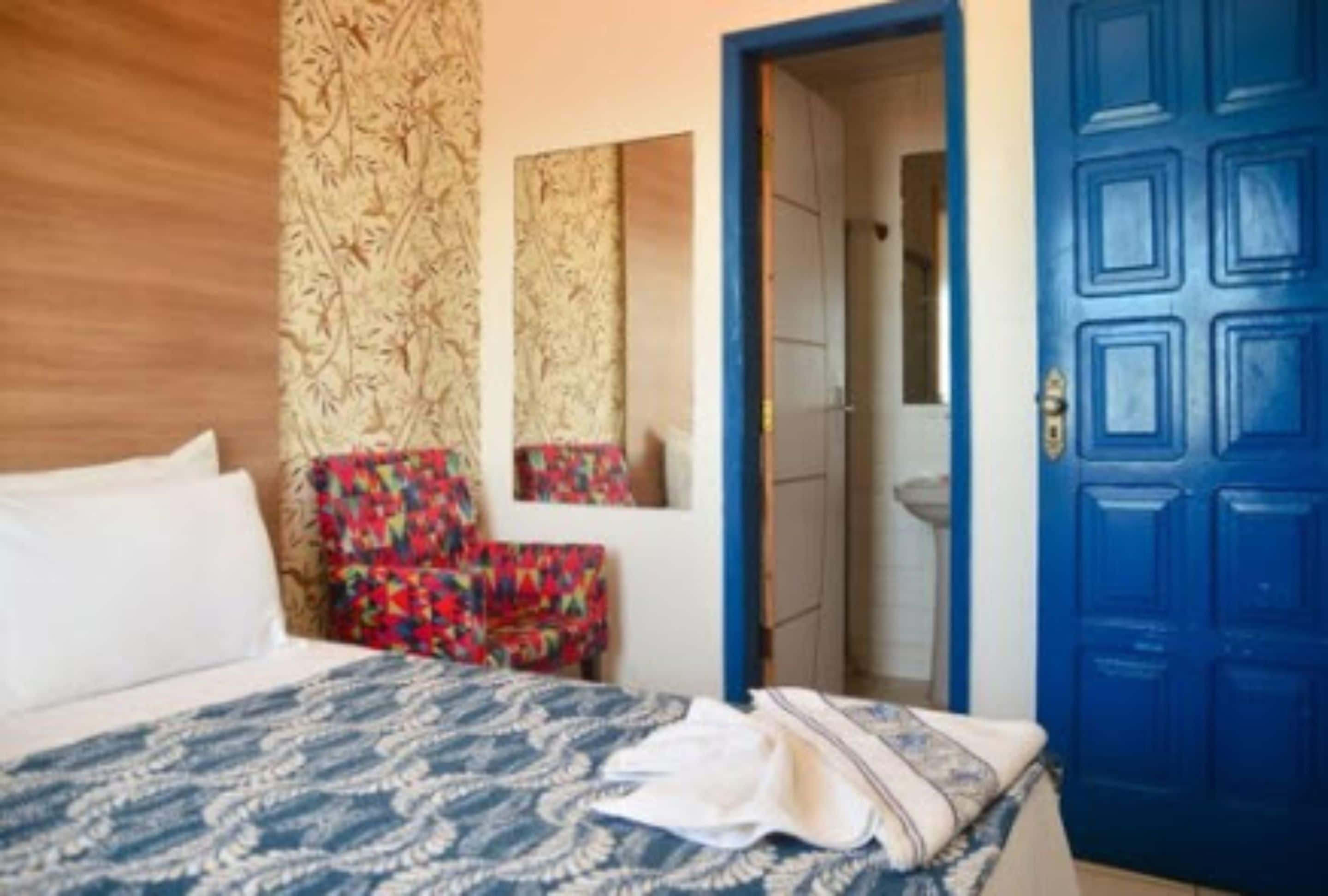 Un dormitorio con una cama, una puerta azul, un espejo y un papel tapiz estampado.