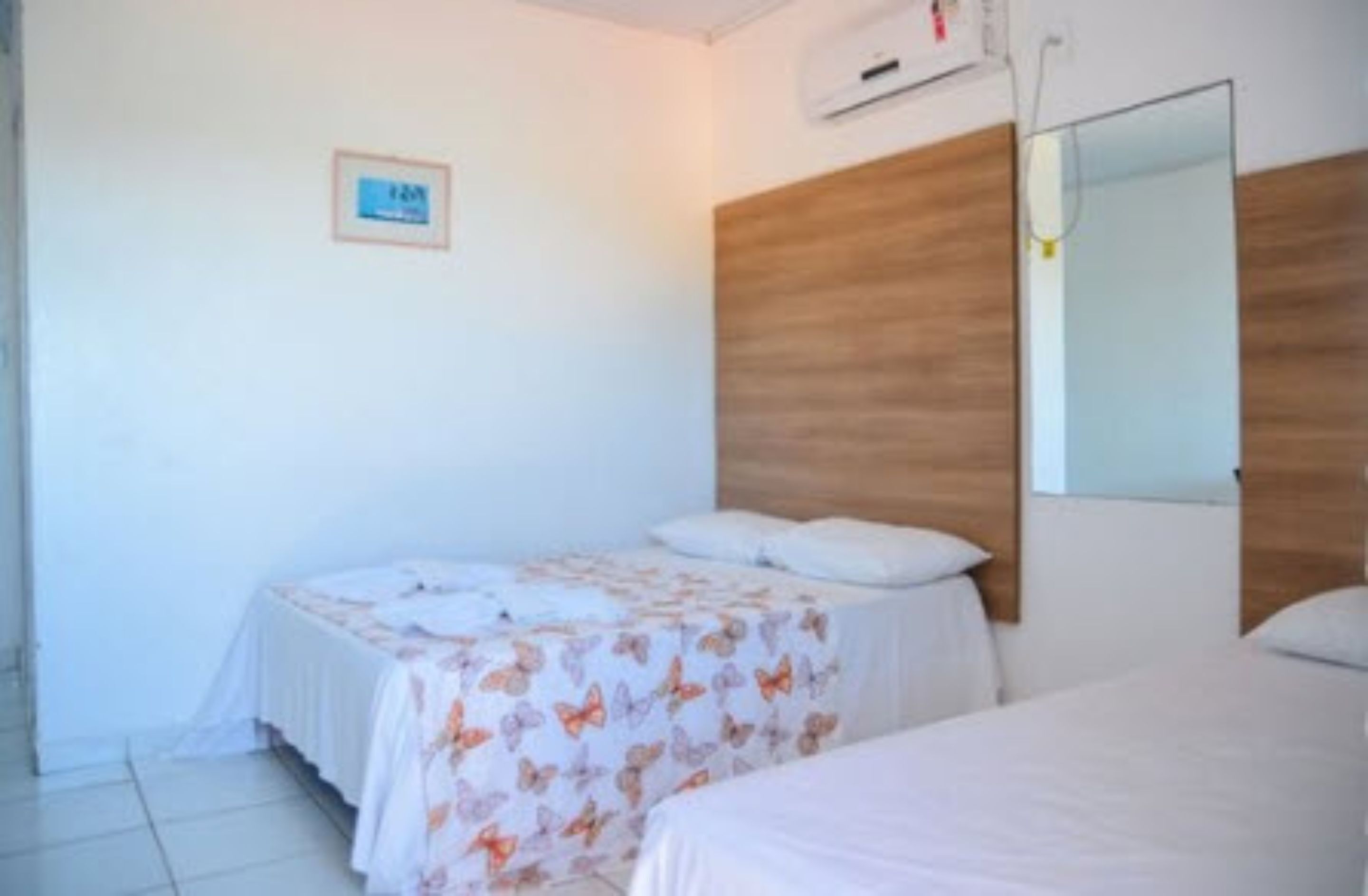 A bedroom with two beds, a wooden headboard, a wall-mounted air conditioner, and a small framed picture.