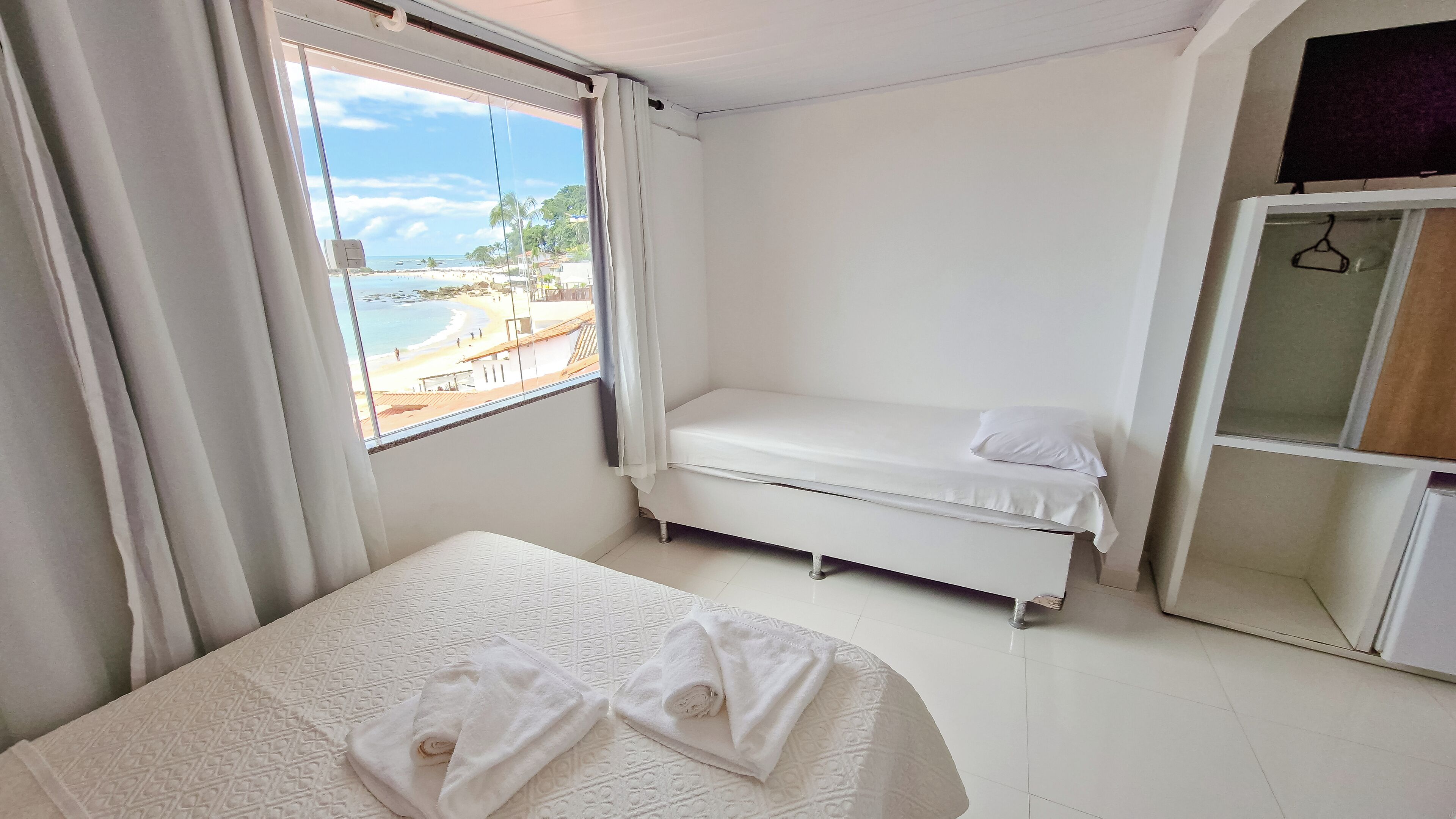 Una stanza piccola e pulita con un letto, una finestra vista spiaggia e un mobiletto.
