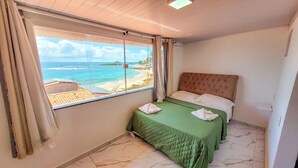 Une chambre d’hôtel avec un lit, une vue sur la plage et une fenêtre avec des rideaux.
