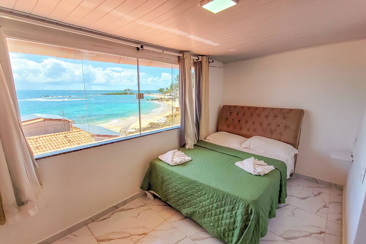 A hotel room with a bed, a view of the beach, and a window with curtains.