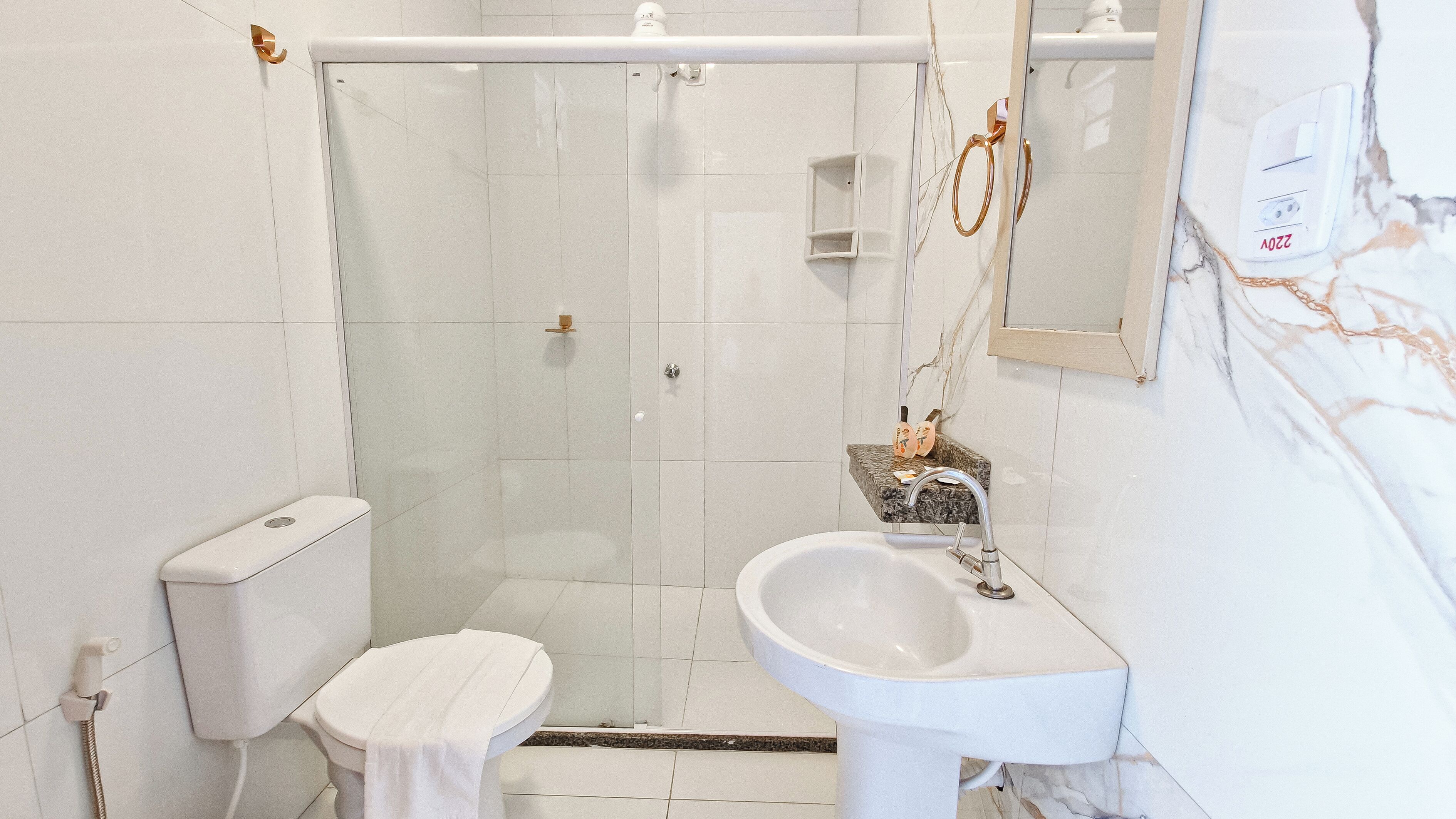 Ein Badezimmer mit einer gläsernen Duschkabine, einem weißen Waschbecken und einer Toilette.