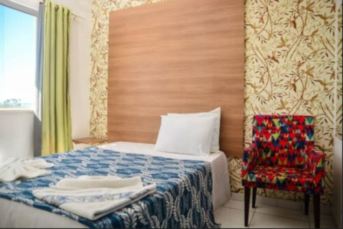 A hotel room with a bed, a chair, and a window with curtains.