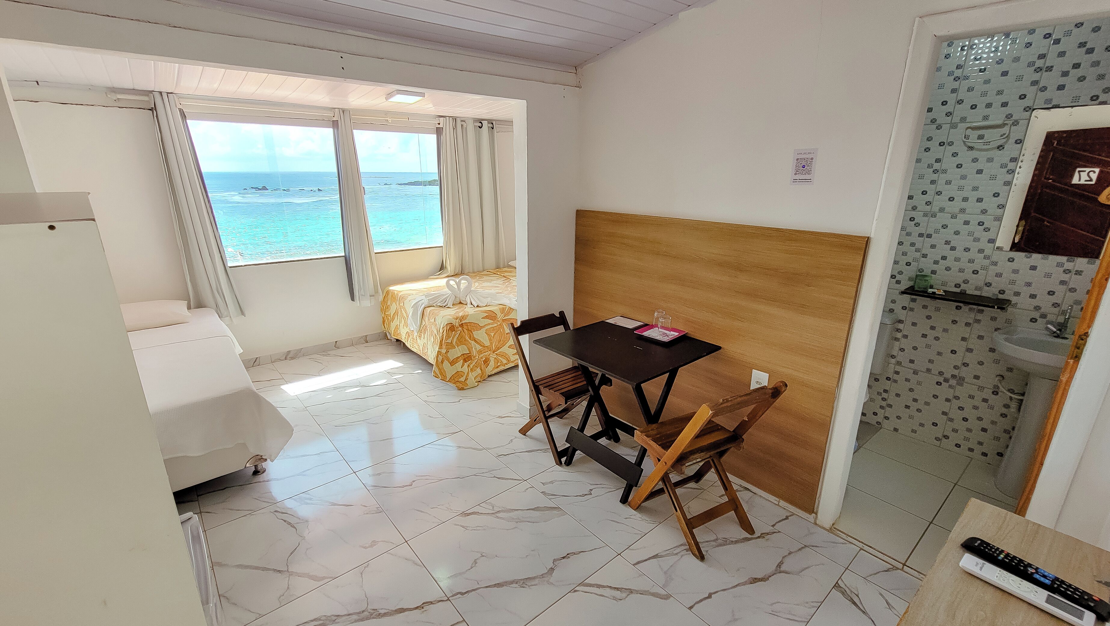 A compact room with a bed, a table, and a view of the sea.