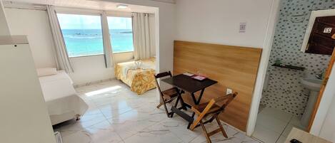 A compact room with a bed, a table, and a view of the sea.