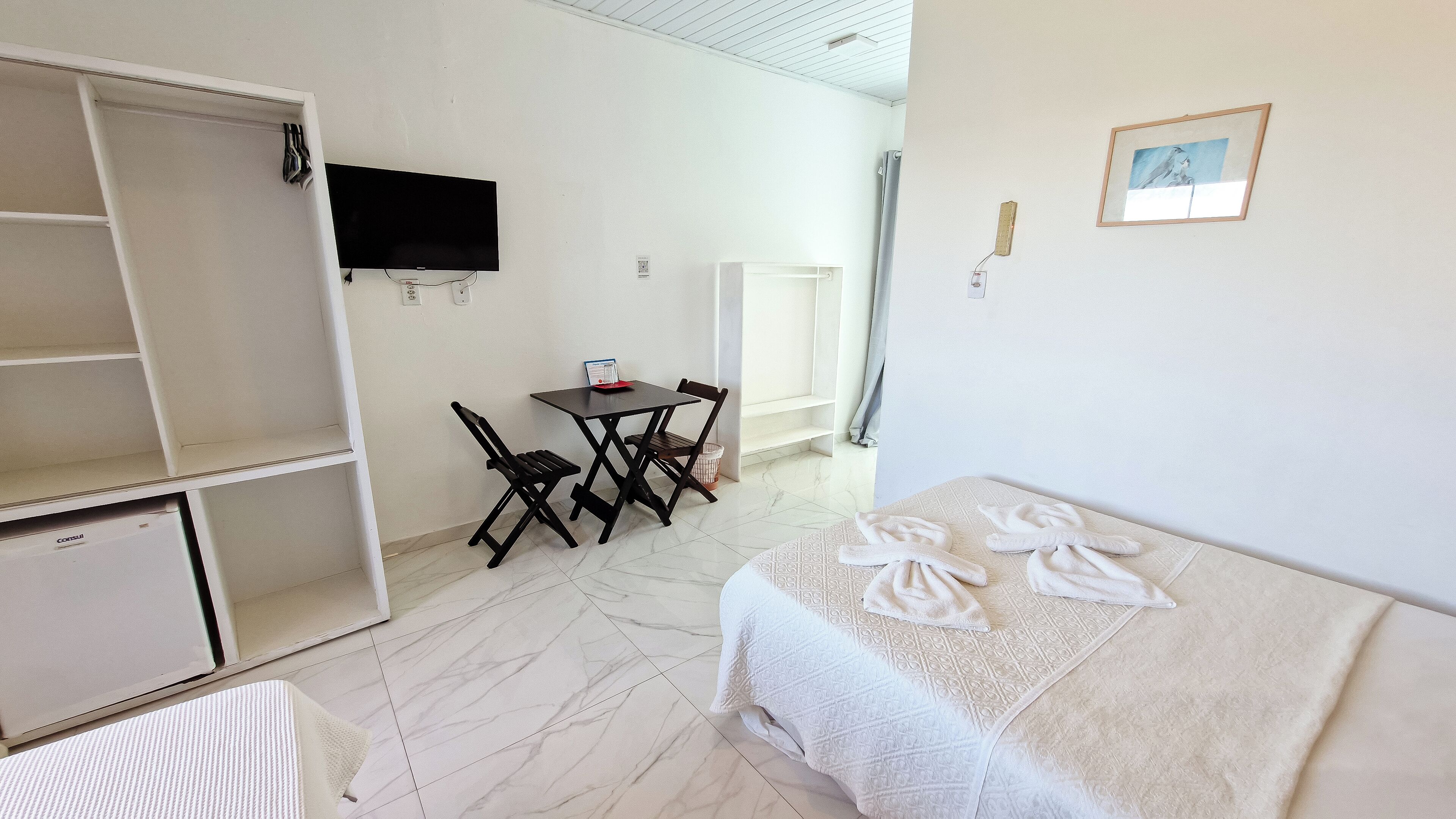 Une chambre comprenant un lit, un bureau avec une chaise, un téléviseur fixé au mur et une armoire.