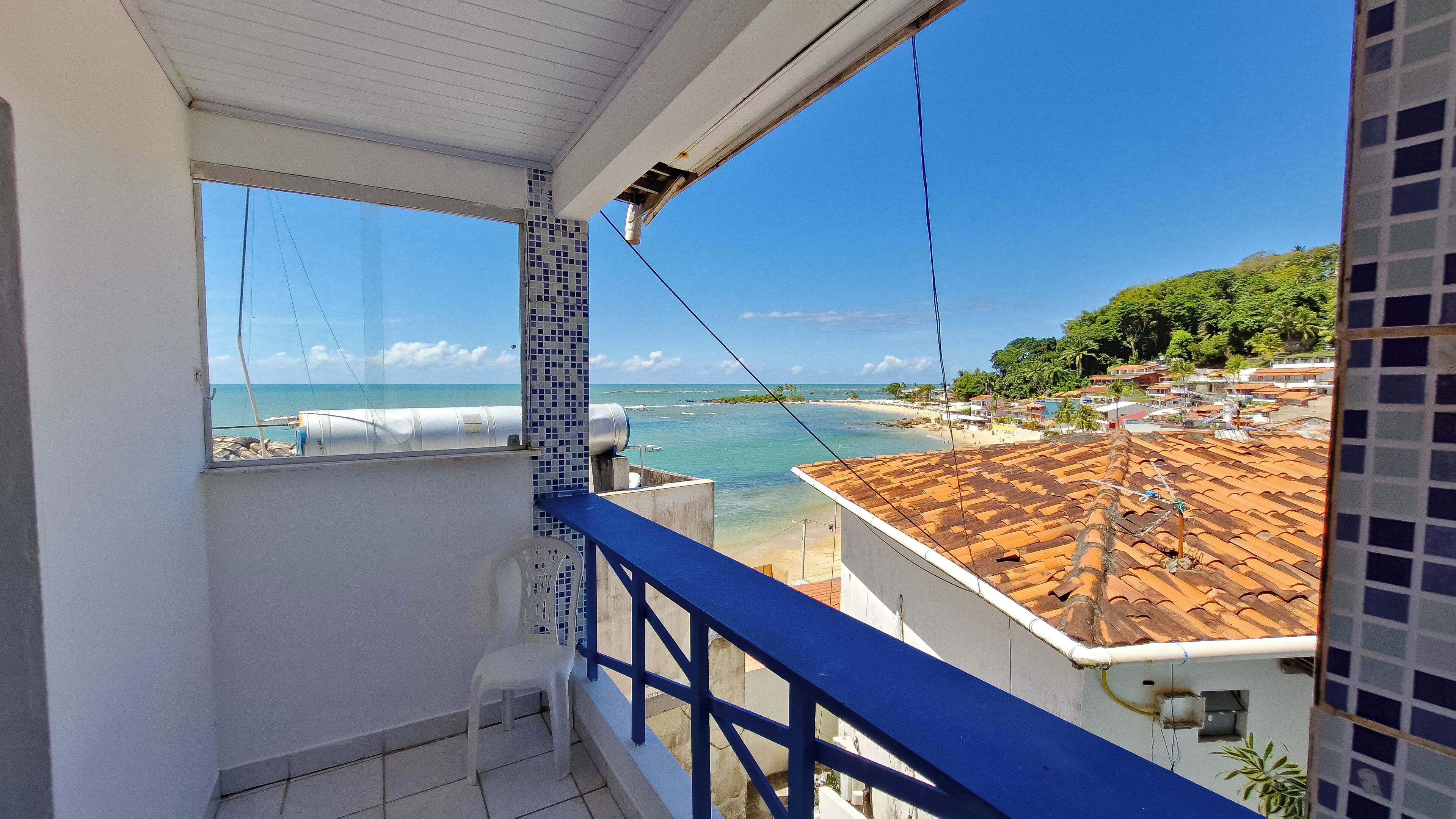 Un balcón con vista a una playa y al océano, suelo de baldosas y barandilla azul.