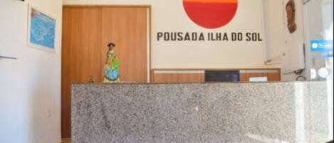 Una recepción con un letrero que dice "POUSADA ILHA DO SOL" y una mujer de pie detrás.