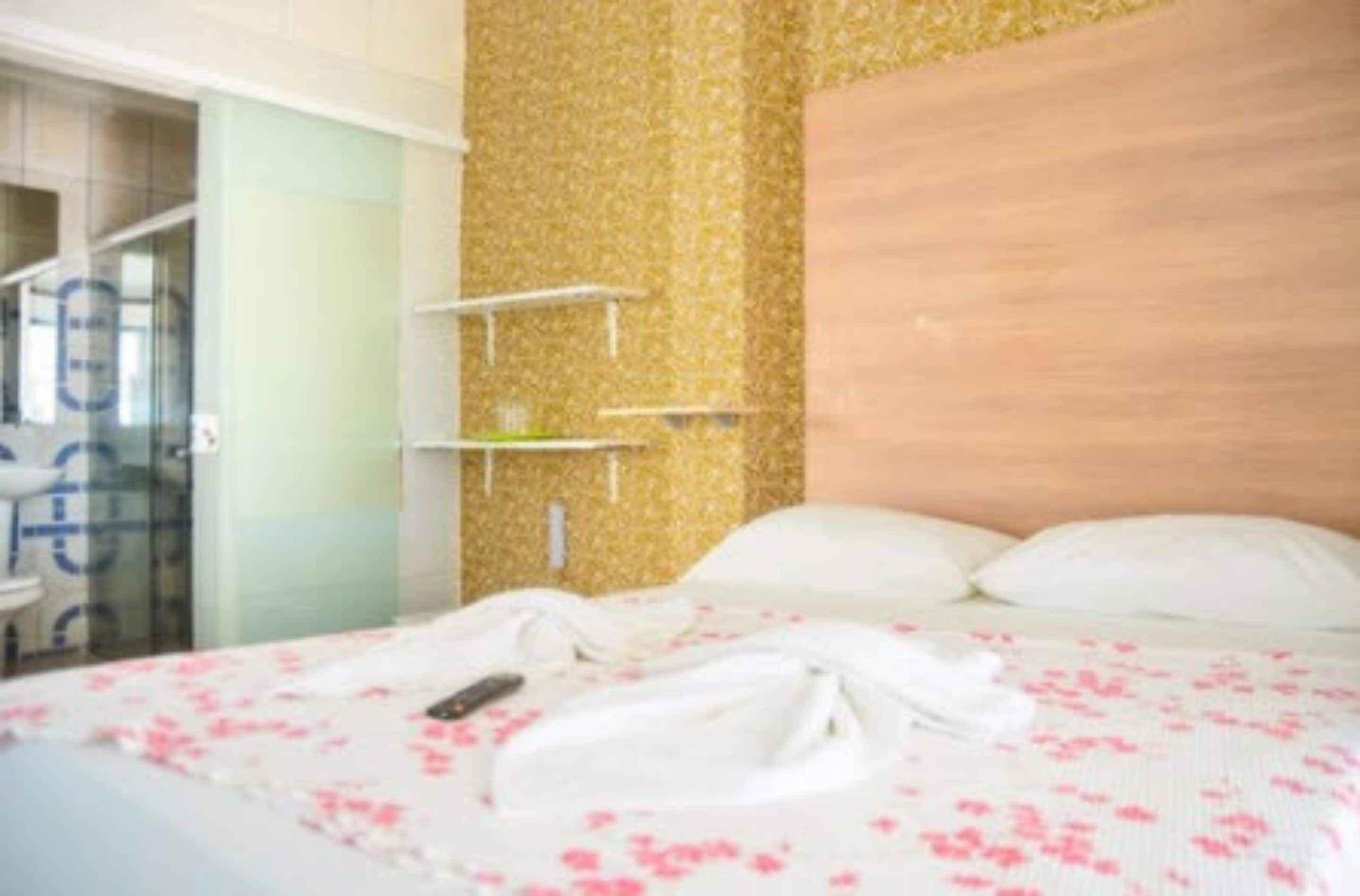 A hotel room with a bed, a wooden headboard, and a small white shelf unit.