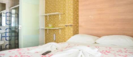 A hotel room with a bed, a wooden headboard, and a small white shelf unit.