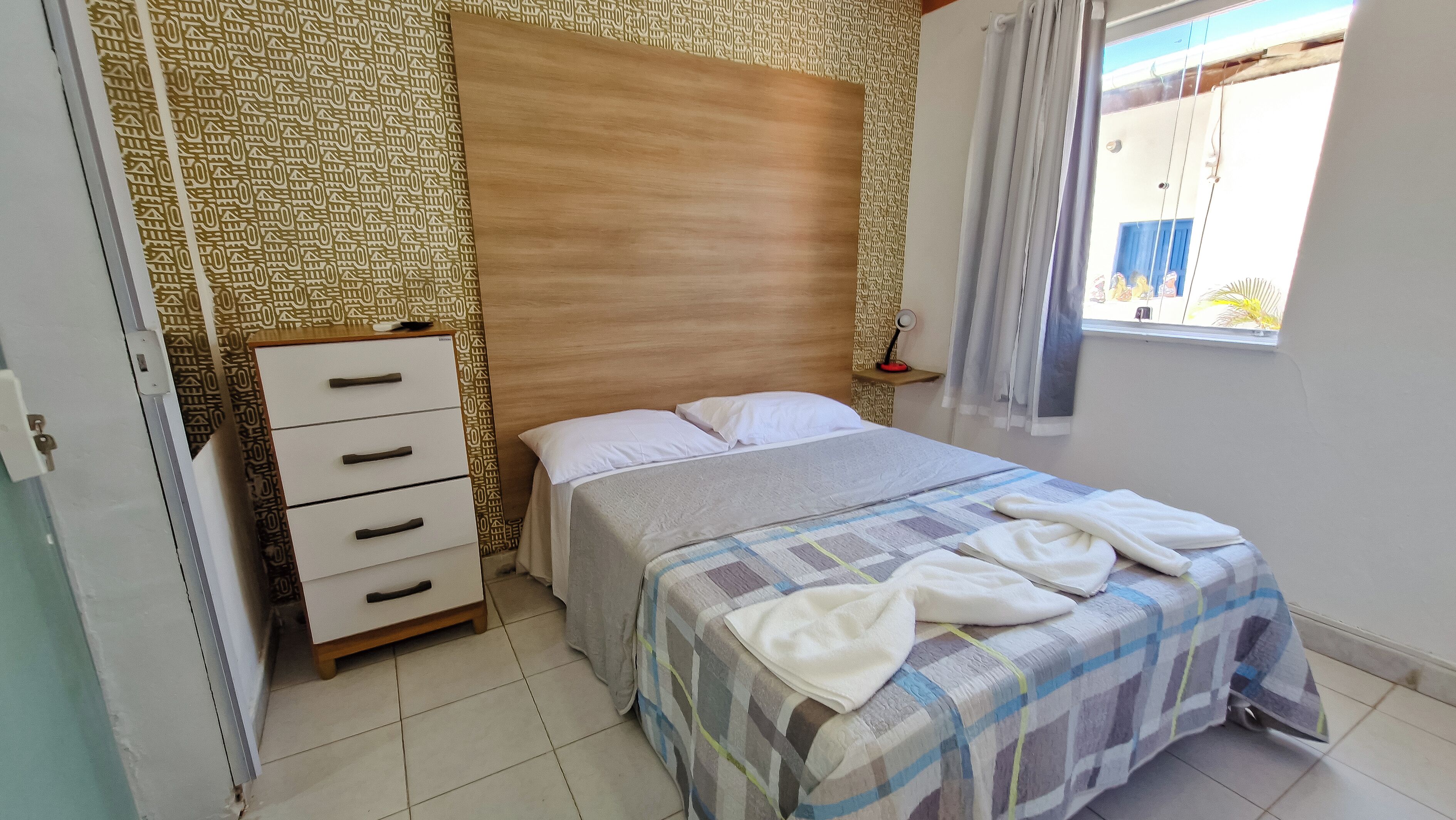 Une chambre à coucher comprenant un lit, une table de chevet, une armoire et une fenêtre avec des rideaux.