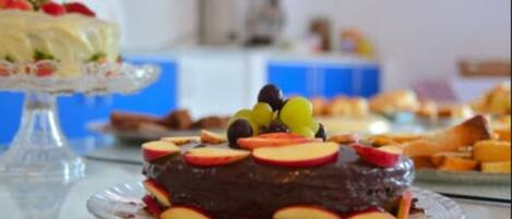 Una mesa de postres con pastel de chocolate cubierto de fruta, un pastel blanco con fresas y diversas pastas.