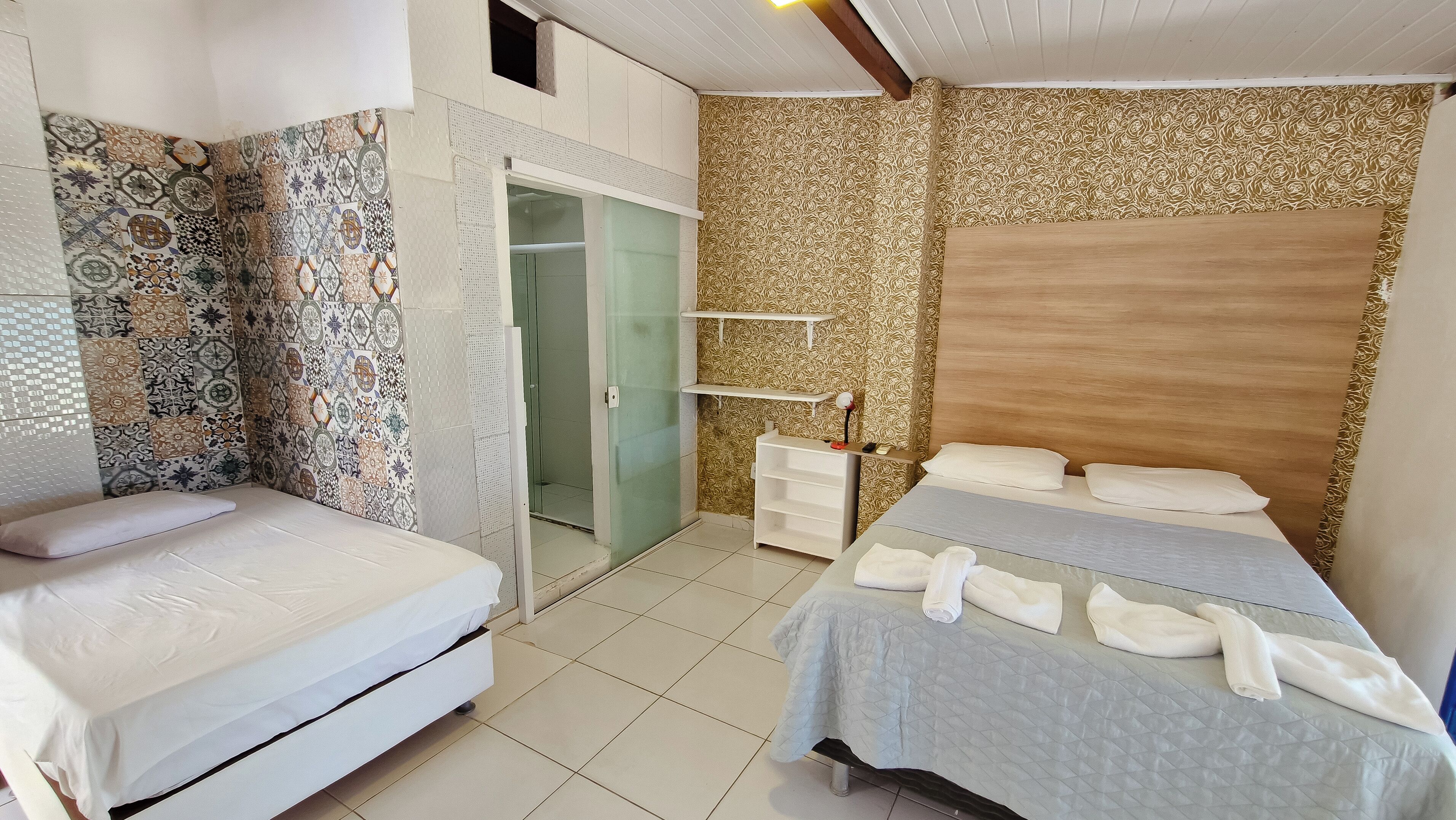 A hotel room with two beds, a wardrobe, a vanity with a mirror, and patterned wallpaper.