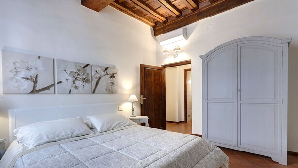 Un dormitorio con cama, paredes blancas, techo de madera, armario y obras de arte en la pared.
