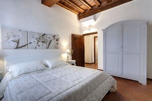 A bedroom with a bed, white walls, a wooden ceiling, a wardrobe, and wall-mounted artwork.