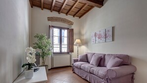 Una sala de estar con un sofá morado, una mesita auxiliar blanca con una planta, una lámpara y una ventana con vistas.