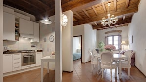 Una cocina con armarios blancos, una estufa y un comedor con sillas y una mesa blancos.