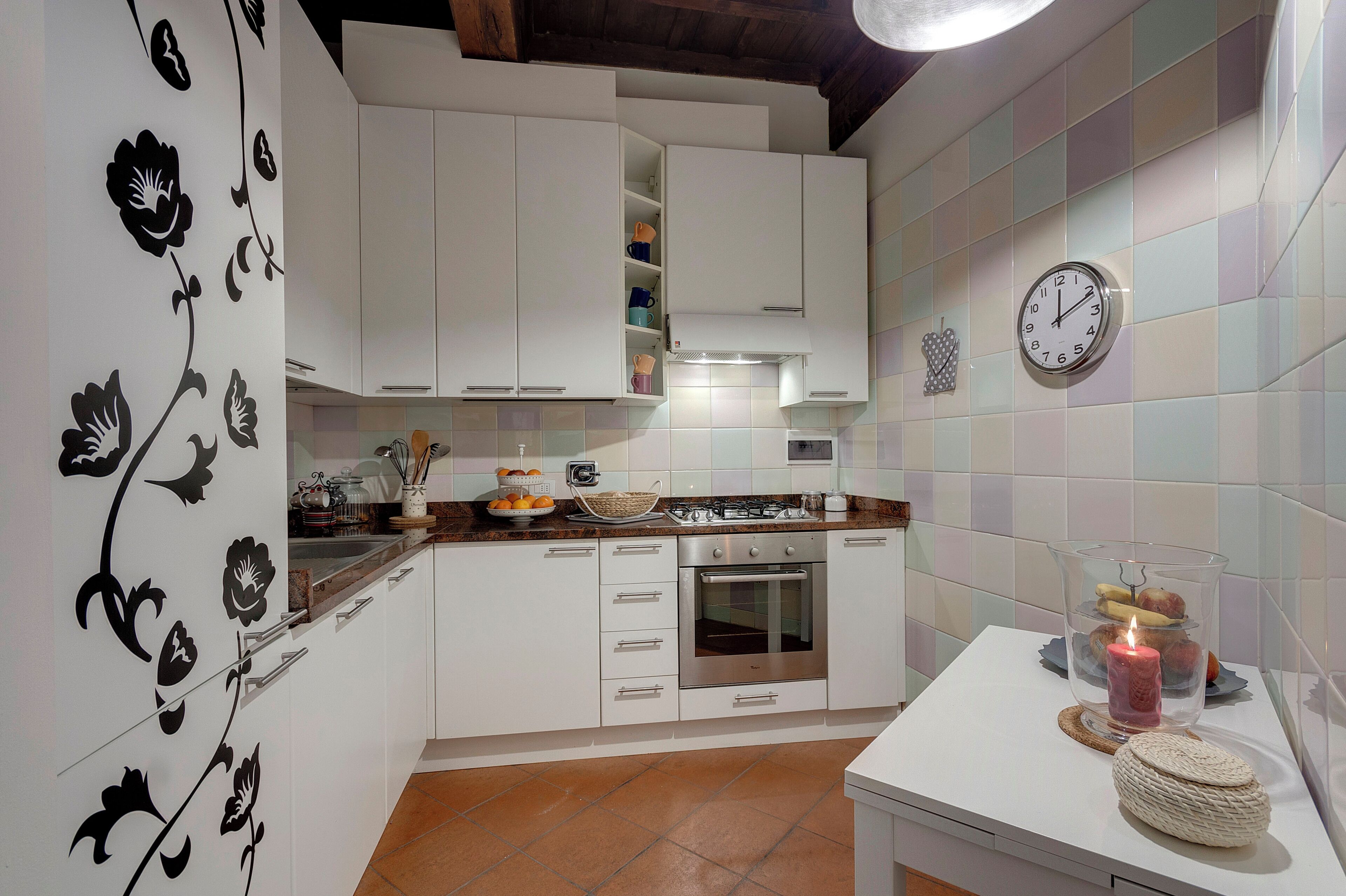 A modern kitchen with white cabinets, a gas stove, an oven, and a clock on the wall.