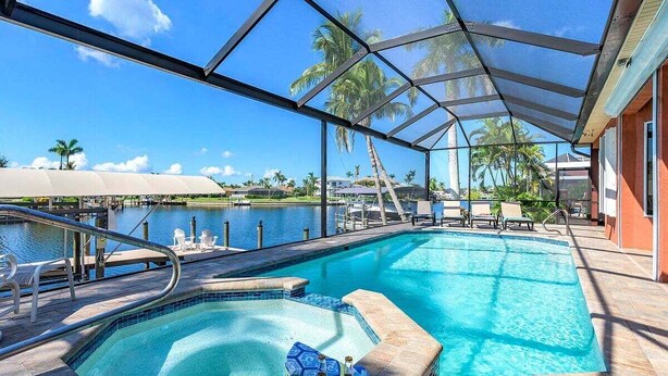 A pool area with a hot tub, lounge chairs, and a view of the water.