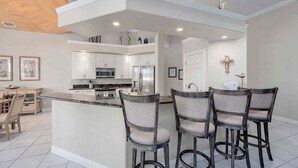 A modern kitchen with white cabinets, a central island with bar stools, and a dining area with a table and chairs.