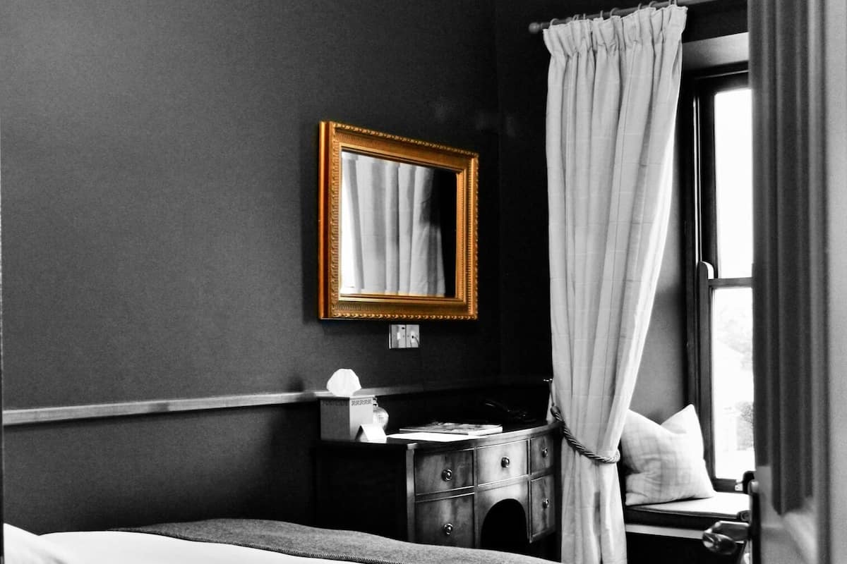 A bedroom with a bed, a dresser, a mirror, and a window with curtains.