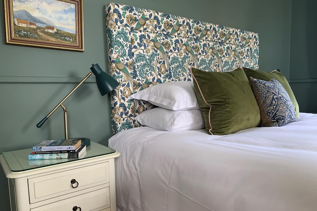 A neatly made bed with white bedding, a floral-patterned headboard, and several pillows.